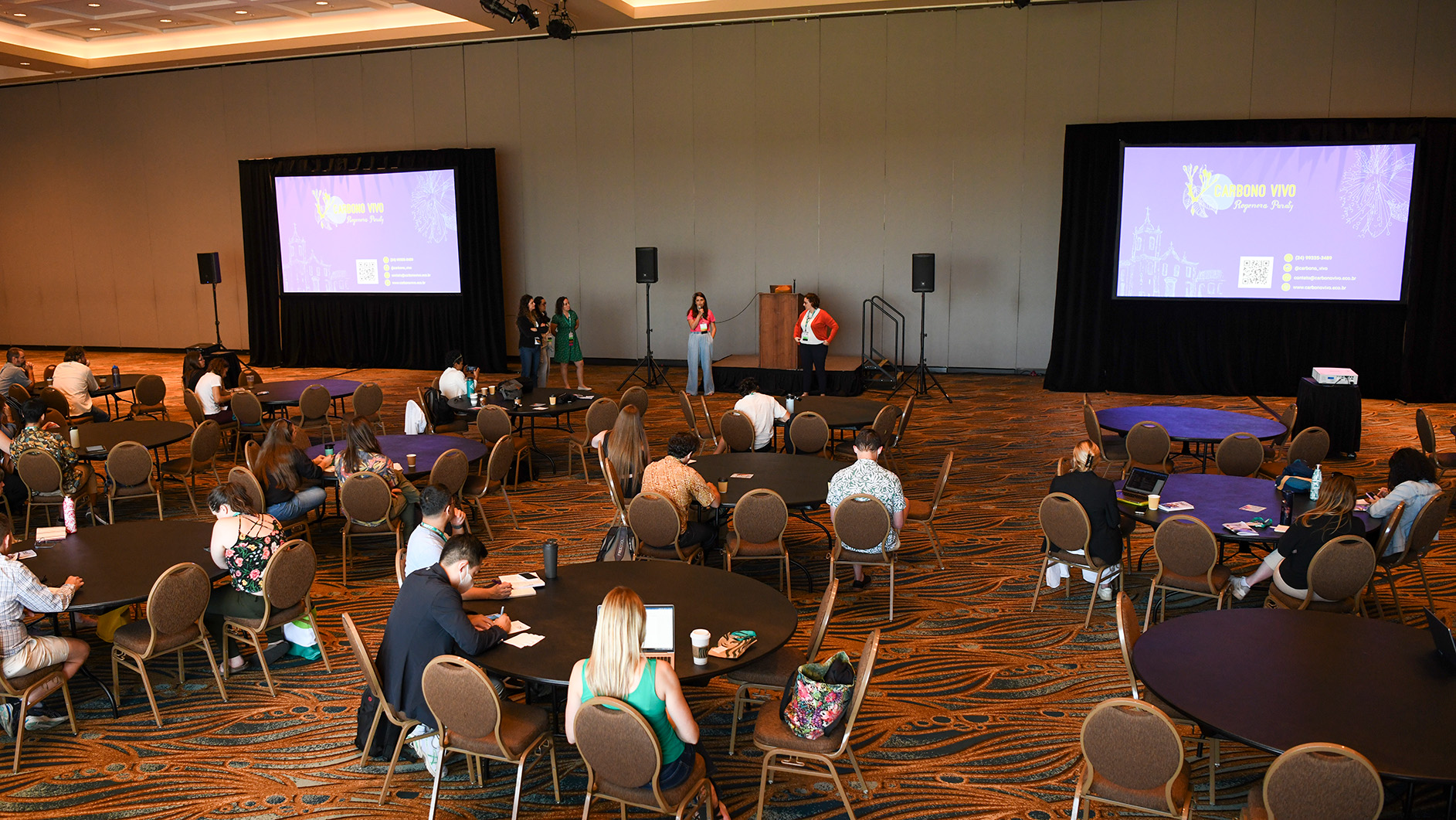 A group of attendees participates in a session with five speakers.