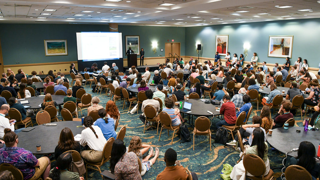 A presenter speaks before a packed room.