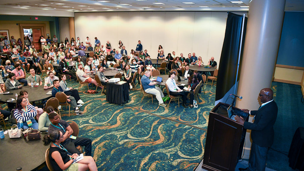 Overhead view of a speaker presenting before a crowded session hall.