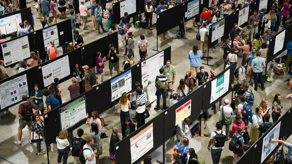 A large group of presenters show off their ideas and findings at a poster session in the main hall.