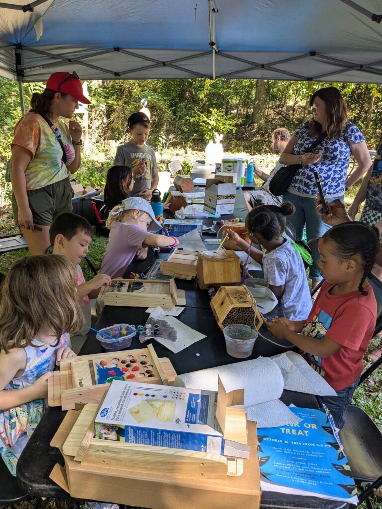 A group of children decorate bee houses at an outdoor table.