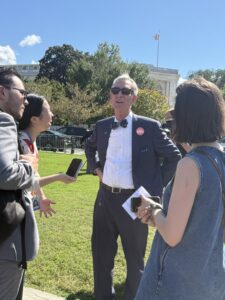 A man in a suit and bowtie speaks to reporters.