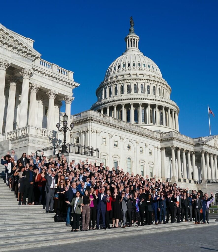 A large group stands on the Capitol steps.