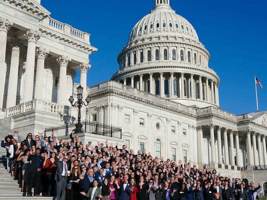 A large group stands on the Capitol steps.