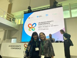 Two smiling people stand in front of a stage with a screen behind them showing "UN Biodiversity Conference"