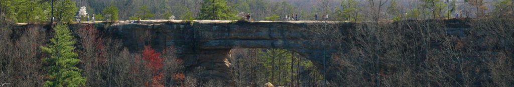 The natural bridge is a kentucky national park. Here we see from a distance a number of people crossing the rock structure. A truly natural bridge.