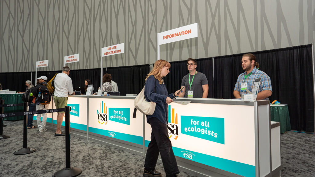 An attendee at the registration desk asks a question of a volunteer.