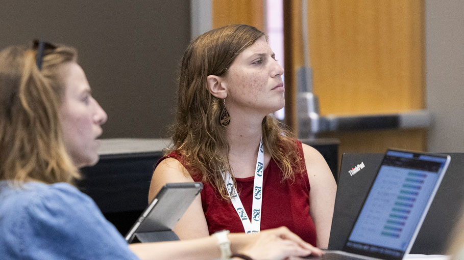 Two women attending the meeting listen intently to a speaker. 