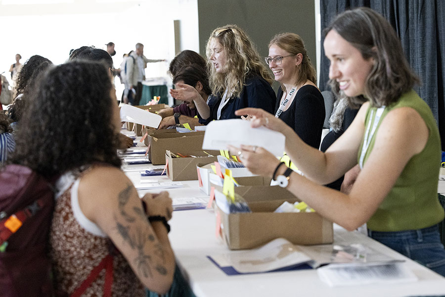 A student volunteer sorts through registration packets for a waiting attendee. 