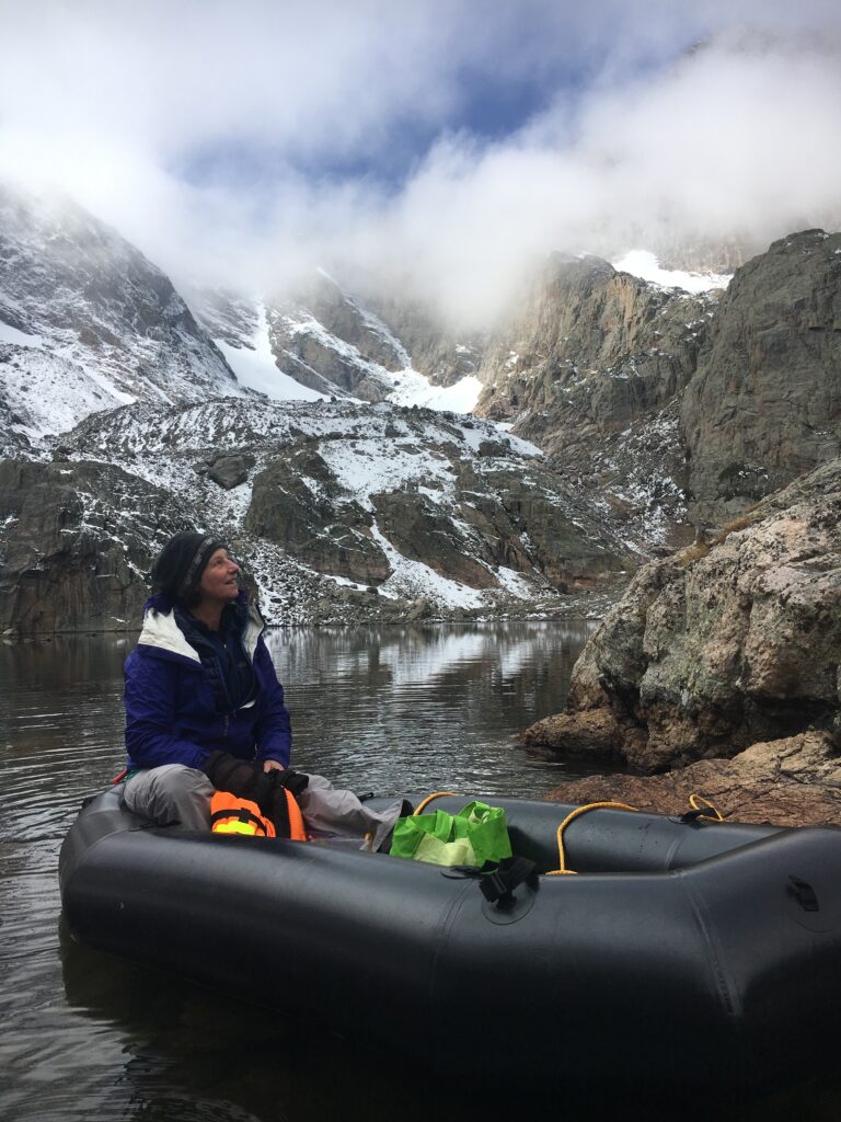 Image of Jill Barron exploring a body of water flanked by mountains while seated in an inflatable boat. 