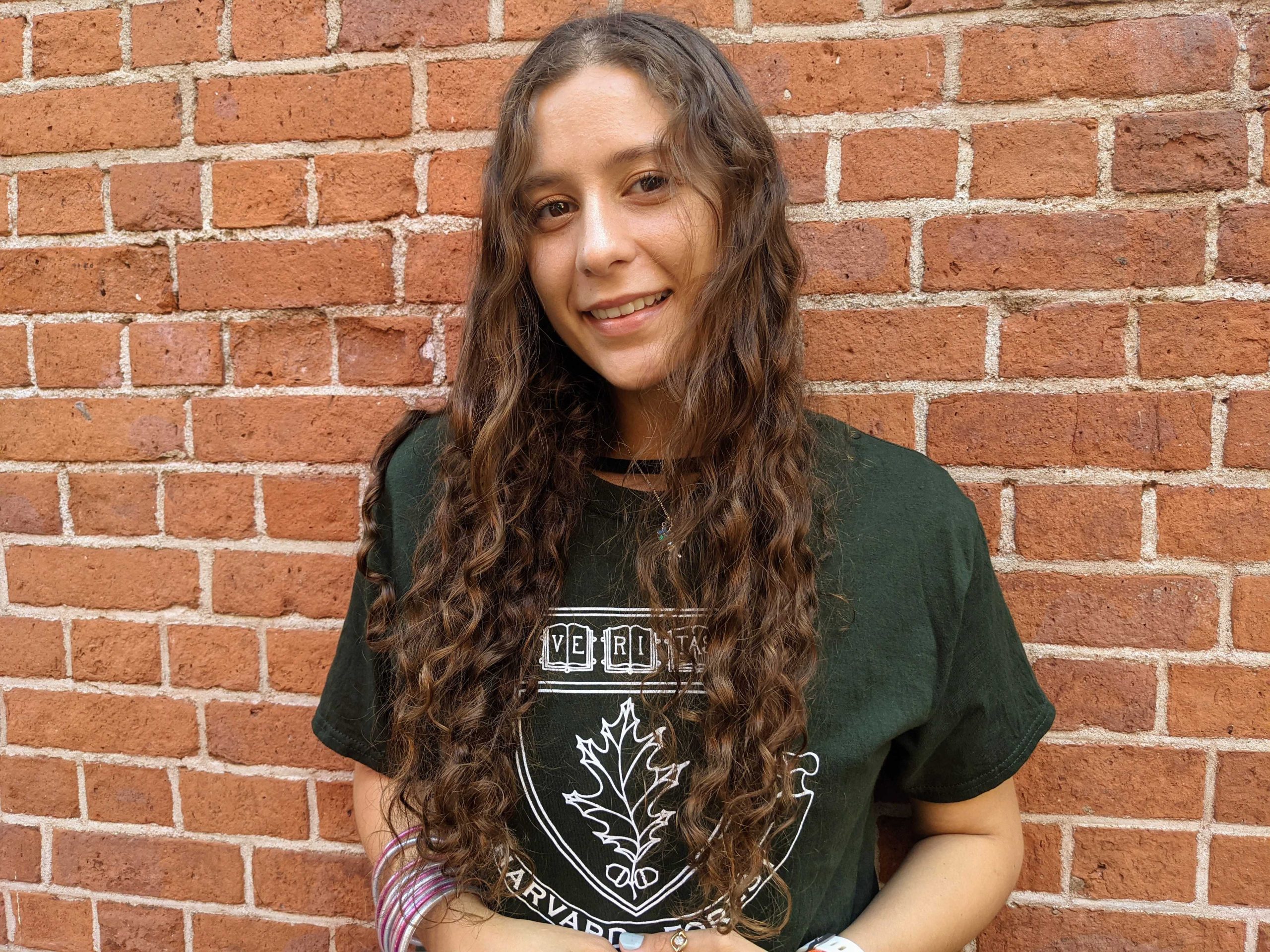 Coral del Mar poses for a photo in front of a brick wall with hands folded.