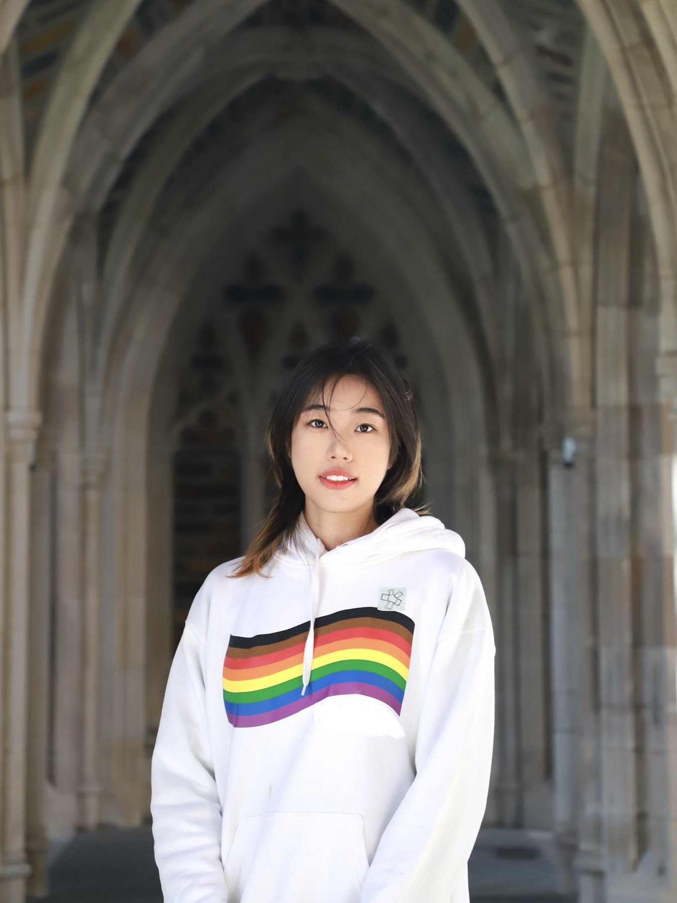 A member of the student sections stands wearing a rainbow hoodie.