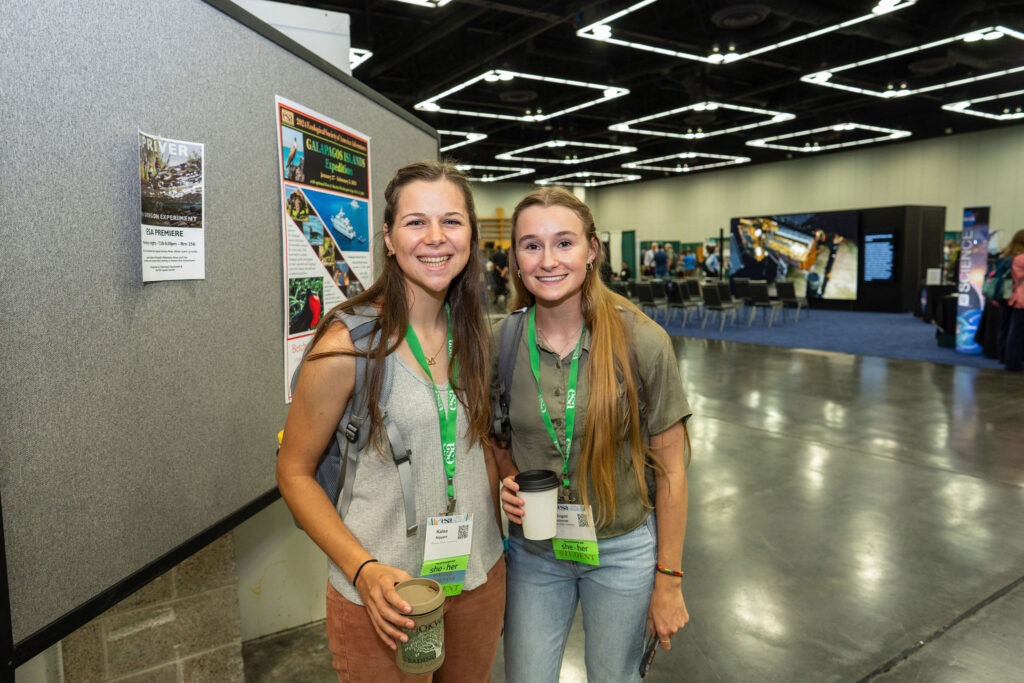 Two women ecologist stand next to each other in the convention center exhibit hall.