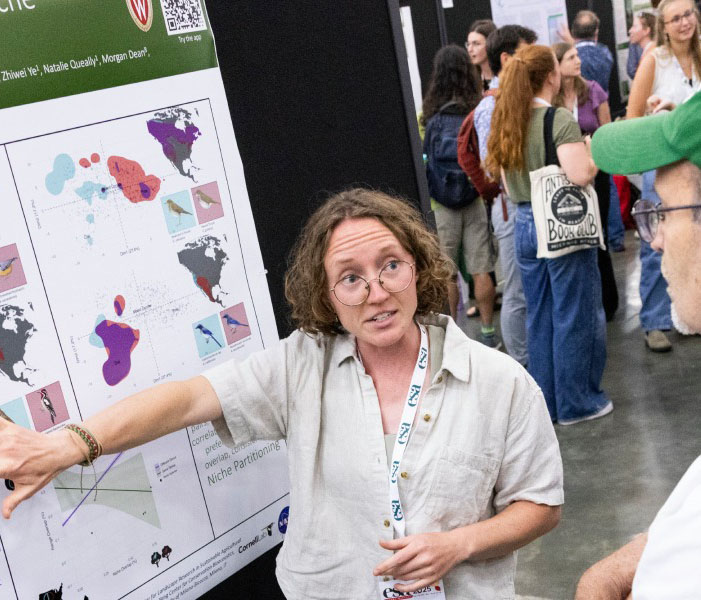 A scientist shares her findings during a poster session with a few onlookers.  Her poster includes data from around the world. 