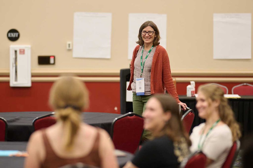 A speaker stands before a group of attendees. All are smiling.