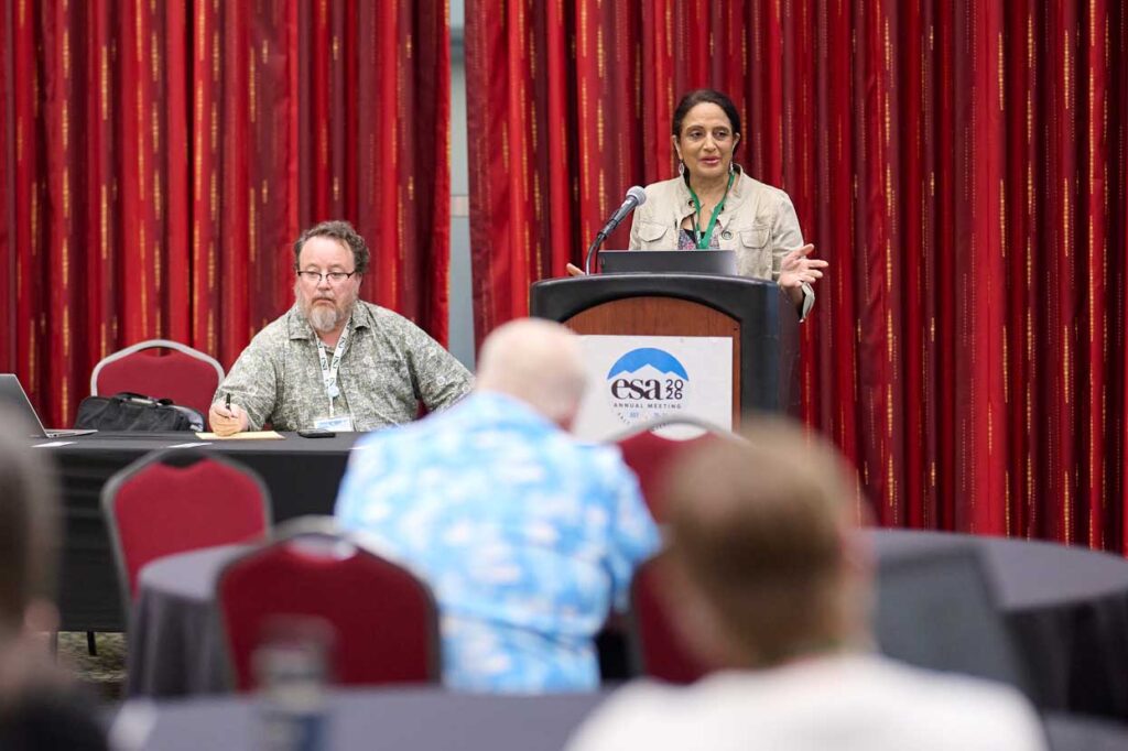 Two speakers, one at a podium, address the audience.