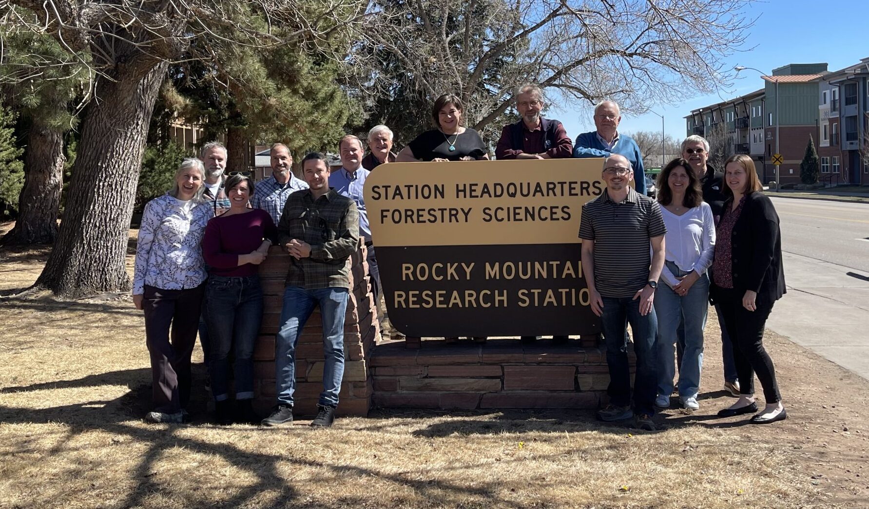 A group poses by a large sign which has "Rocky Mountain Research Station".