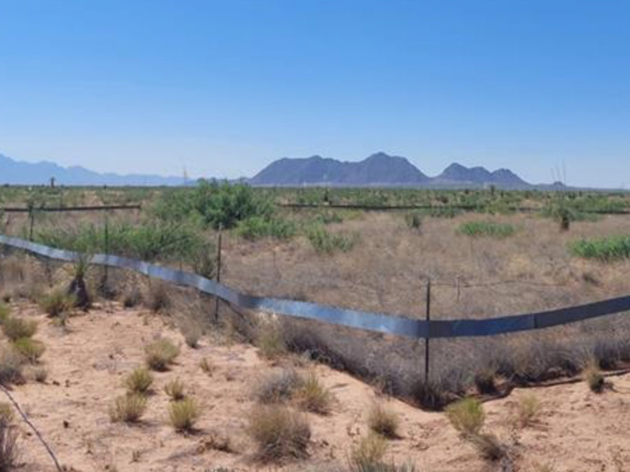 An arid landscape with a fenced enclosure in the foreground.