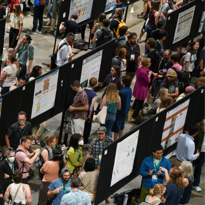 an overhead view of a poster session at the 2024 Annual Meeting -- the space is jam-packed with presenters and hundreds of others in to see their works. It is very exciting!