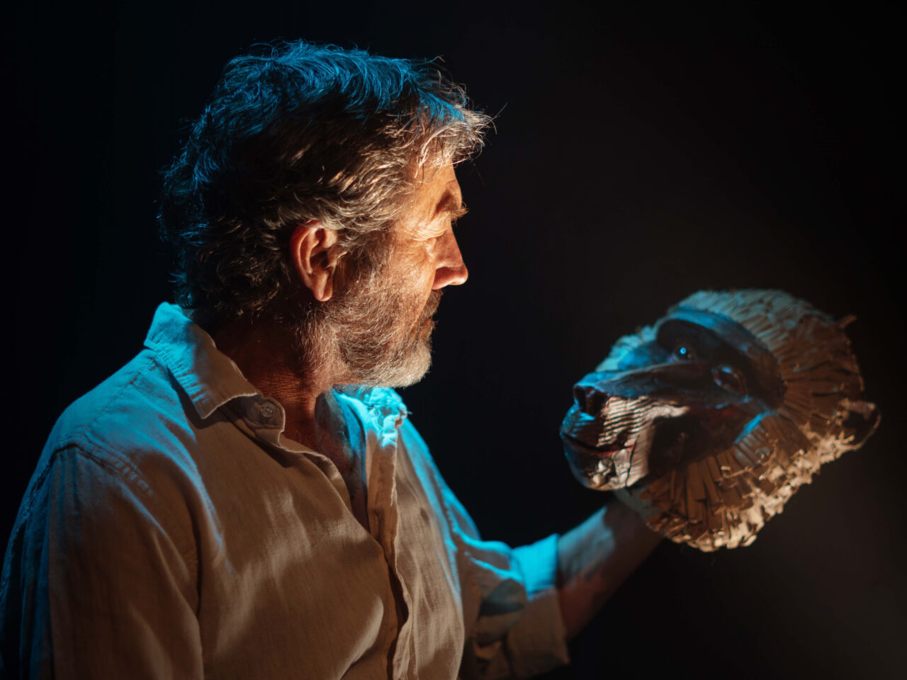 An actor holds a baboon mask