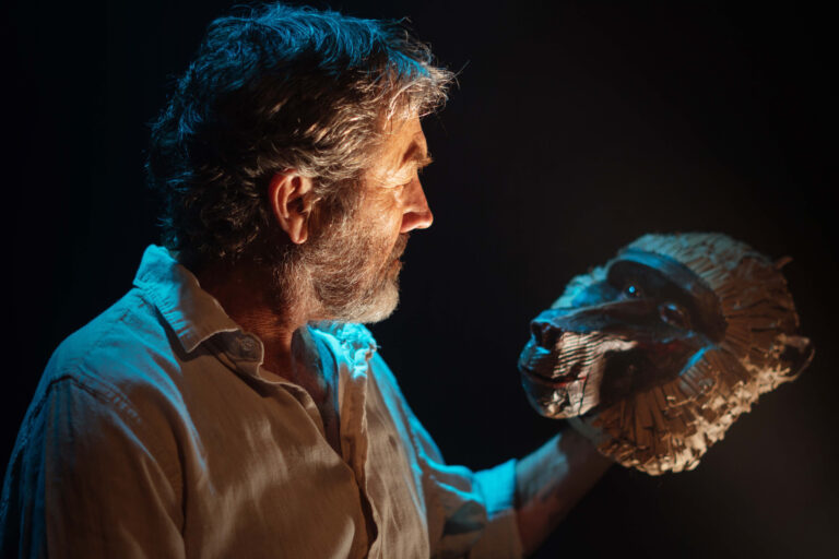 An actor holds a baboon mask