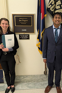 Two people in suits holding ESA folders stand in front of a congressional office