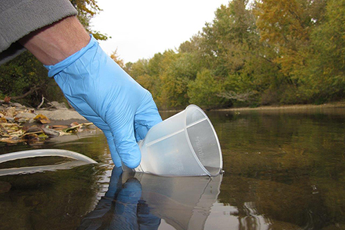 A gloved hand scoops water from a river